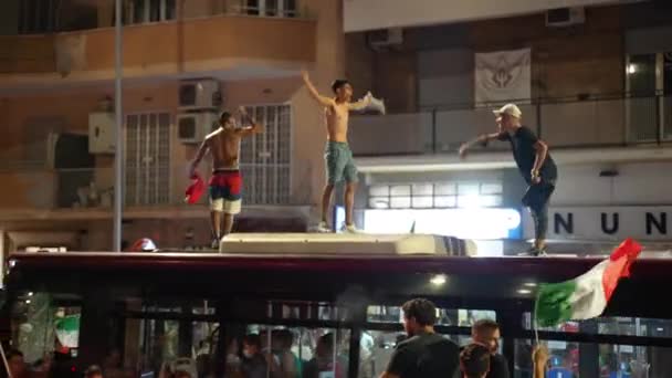 ROME, ITALY - 2021 년 7 월 11 일 : T 셔츠가 없는 거리 이탈리아 훌리건들 축구 국가 대표 팀의 승리 이후나쁜 행동을 하고 있다 EURO 2020, 술취한 남자들 이 버스 지붕에 올라가 손을 흔들며 소리를 질렀다. — 비디오