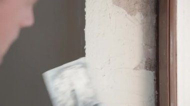 İnşaat alanında çalışan tamirci, erkek müteahhit metal spatula kullanarak duvar ve açıları spatula ile kaplıyor. Duvarların hizalanması, mühendislik konsepti