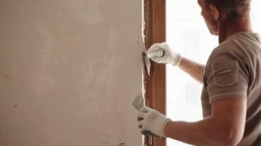 Yapı işçisi, alçı işleri için profesyonel aletler ve aletler kullanıyor, duvar yüzeyini metal spatula ve macunla hizalayıp düzleştiriyor. Mühendislik endüstrisi, restorasyon