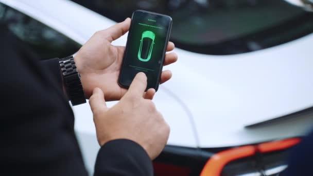 RZYM, WŁOCHY - KWIECIEŃ 28, 2021: Biznesmen trzymający smartfona i pokazujący funkcję autopilota elektrycznego samochodu Tesla klasy premium, człowiek włączający reflektory samochodowe i uruchamiający je na autopilota — Wideo stockowe