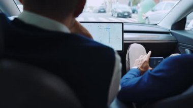 Başarılı bir işadamı yüksek teknolojili Tesla arabasıyla şehir merkezinde araba sürüyor. Yanında erkek arkadaşı, direksiyon başında, arkadaşlarıyla konuşuyor, arka planda el kol hareketi yapıyor.