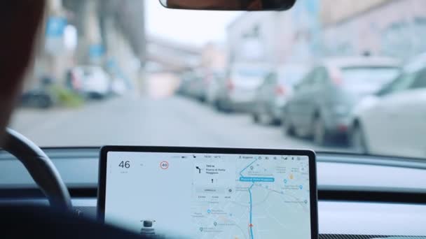 Успешный бизнесмен едет по центральной улице на высокотехнологичном электрическом автомобиле Тесла Модель 3, человек рулевое колесо и с использованием переднего сенсорного дисплея с различными функциями, приложениями и навигации — стоковое видео