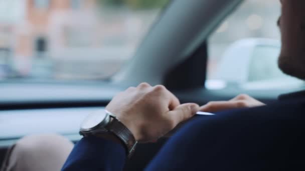 Exitoso hombre de negocios que conduce a lo largo de la calle del centro en el coche Tesla eléctrico de alta tecnología Modelo 3 con conductor, hombre concentrado sosteniendo el teléfono inteligente en las manos y mirando en la carretera. Coche autónomo de nuevo — Vídeo de stock