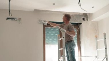 Yeni apartmandaki inşaat sahasında tamirat çalışmaları merdiven üzerinde duran ve pencerenin etrafındaki duvarları dış perdelerle kaplayan bir bina ustası. Metal spatula kullanan işçiler