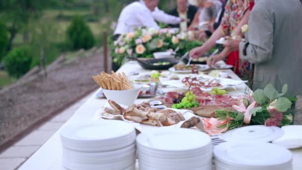 Ozdobiony stół w formie bufetu ślubnego ze świeżymi bukietami kwiatów i różnorodnością smacznych włoskich plastrów prosciutto, kotletów serowych, owoców, przekąsek, kanapek i przystawek rybnych. Goście weselni degustacja tradycyjnych — Wideo stockowe