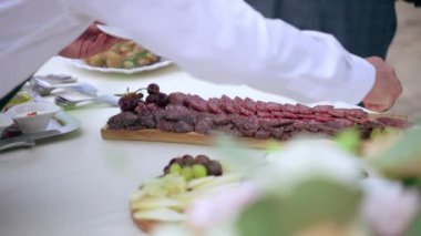 Lüks düğün partisinde konuk ağırlayan üniformalı garson tabağa salam dilimleri koyan hizmetçi peynir pirzolası ve diğer lezzetli aperatifler. Üst düzey yemek servisi...