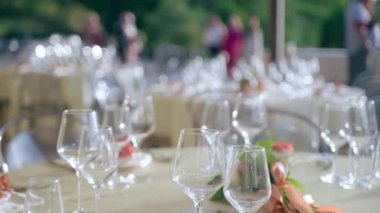 Wedding festive tables decor on blurred invited guests background, elegant round tables served with ivory napkins, heart shape placeholders, wine, champagne and water glasses, and flowers bouquet in