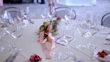 Beautifully organised round tables arrangement on wedding party, crystal wine and champagne glasses with silver cutlery on ivory tablecloth. Fresh flowers bouquet with apricot ribbon in the middle of