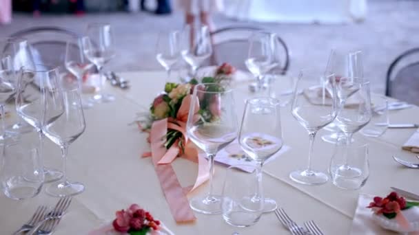 Beautifully organised round tables arrangement on wedding party, crystal wine and champagne glasses with silver cutlery on ivory tablecloth. Fresh flowers bouquet with apricot ribbon in the middle of — Stock Video
