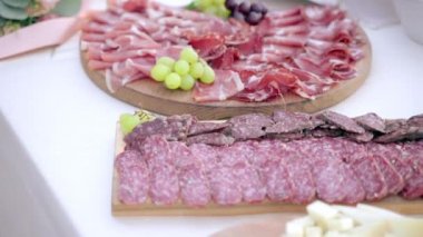 Tasty juicy Italian prosciutto, salami and cheese slices on wooden board on buffet table, traditional Italian cuisine on luxury wedding parties celebrating outdoors in ancient restaurants. Elegant