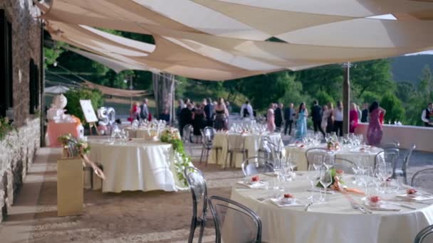 Blurred wedding guests waiting for married couple on foreground of served festive tables decor. Beautiful round tables decorated with flowers bouquets and elegant tableware and cutlery. Wedding party — Stockvideo