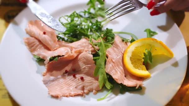 Lüks beyaz tabak, roket salatası, limon suyu, portakal dilimi ve baharatlı soslu egzotik somon dilimleri. Akdeniz 'i tatmak için gümüş bıçak ve çatal kullanan bir kadın. — Stok video