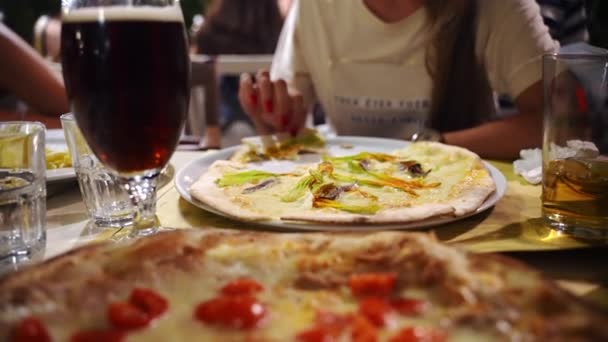 Mulher irreconhecível degustando pizza italiana suculenta com queijo derretido, pimenta, ervas e flores de abobrinha, e bebendo cerveja vermelha para refrescar após o dia de trabalho duro. Pizzaria italiana tradicional — Vídeo de Stock