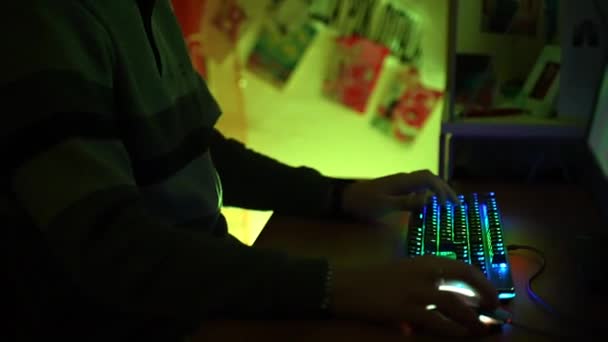 Jugador de ordenador sentado en la mesa en la sala iluminada de color amarillo y la celebración de torneos en línea con jugadores virtuales en el ciberespacio utilizando el teclado retroiluminado espectro y el ratón. Concursos en línea para la diversión — Vídeo de stock