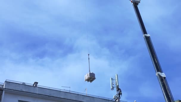 Bulutlu gökyüzü arkaplan üzerinde inşaat vinci. 5G kule anteninin montajı için konut binasının tepesindeki telekomünikasyon ekipmanlarını kaldırıyor. Telekom işçileri mühendislik ekipmanlarını... — Stok video