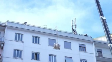 Dünyadaki küresel iletişim gelişimi, 5G kulesi kurmak için İtalya 'da inşaat alanında çalışan telekom işçileri. Mühendislik vinci binanın tepesindeki hücresel istasyon ekipmanlarını kaldırıyor.