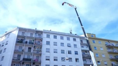 İtalya 'da gökyüzü arka planındaki yüksek binaların düşük açılı görüntüsü, daha iyi sinyal iletimi için 5G kulesi kurmak üzere binanın çatısındaki endüstriyel vinç kaldırma cihazları