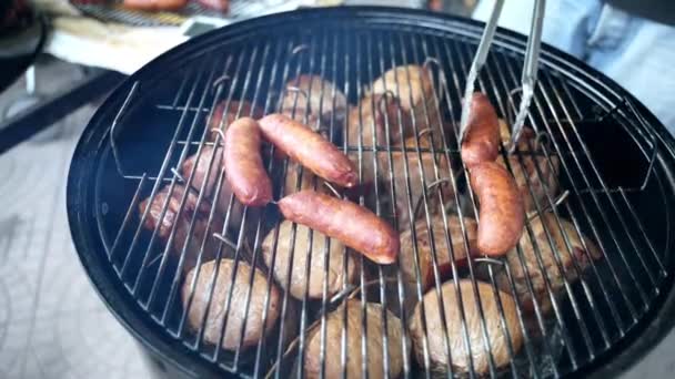 Ovanifrån av läckra saftiga bratwurst korv och kryddiga kycklingben grillning på träkol för Oktoberfest picknick parti, man med matlagning tång för att vända sig rostning kött på bbq grid — Stockvideo