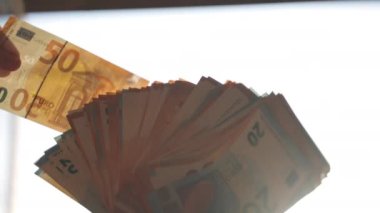 Avro banknotlarını kontrastlı ışıkta tutan kişi, para destesinden banknot çıkaran ve kağıt para levhalarını kontrol eden banka çalışanı. Para geliri, sahte işlemler ve