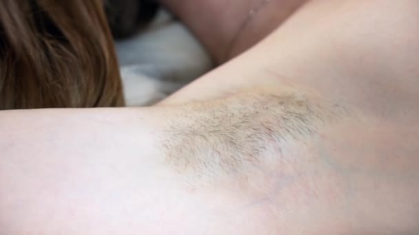 Zbliżenie zdjęcie kobiety pachy z rosnącymi włosami, kobieta leżąca na kanapie salonu przygotowana do zabiegu depilacji woskiem. Nowoczesny trend naturalnego piękna, rosnące włosy pod pachami — Wideo stockowe