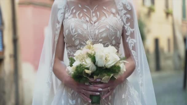 Noiva encantadora no vestido de casamento de renda posando na rua segurando rosas brancas buquê de casamento, mãos de noiva com anel de casamento segurando buquê de flores, flores da cerimônia de casamento em mãos de bonito — Vídeo de Stock