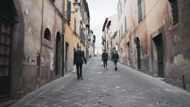 Vedere din spate a cetățenilor italieni care se plimbă de-a lungul străzii medievale înguste vechi, cu exteriorul clădirii caracteristice, clădiri cu fațade ruinate din diferite epoci arhitecturale. Sate italiene antice — Videoclip de stoc