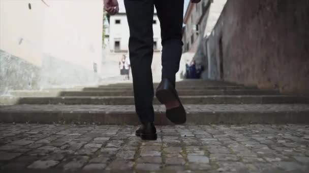 Vue arrière de l'homme en costume élégant et chaussures noires grimpant des escaliers en béton le long de l'ancienne rue, vue rapprochée des pieds des personnes grimpant dans des escaliers au ralenti. Concept de passage de l'homme dans la rue — Video