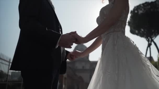 Όμορφο παντρεμένο ζευγάρι κρατώντας τα χέρια στο φως του ήλιου, όμορφη νύφη με δαντέλα νυφικό κοιτάζοντας την υπέροχη γαμπρός, παντρεμένος ζευγάρι ποζάρουν στην κάμερα σε καταπληκτικό ρωμαϊκό φόρουμ φόντο στη Ρώμη — Αρχείο Βίντεο