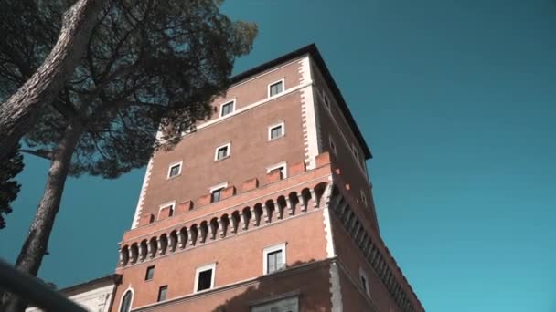 Nízký úhel pohledu na slavnou věž Palazzo Venezia ve slunečním světle na úžasném modrém prohnaném pozadí a rostoucí borovice, charakteristická římská budova fasáda věže v centru Říma, italský — Stock video