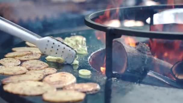 Chef usando pinzas de cocina para darle la vuelta a las verduras asadas en el ahumador de barbacoa, proceso de freír rodajas de papa y cebolla en la quema de carbón vegetal en el fumador, barbacoa a la parrilla preparación en el festival — Vídeo de stock