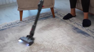 Elektrik süpürgesinin yakın çekimi halının üzerinde hareket ediyor, toz ve enkazı temizliyor. Ev temizleme işlemi.