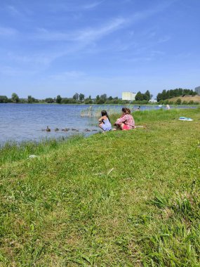 Kızlar ördekleri ve ördeklerini gölün kenarında besler. - Evet. Açık havada güneşli bir hafta sonu. Fotoğraf Belarus 'tan.