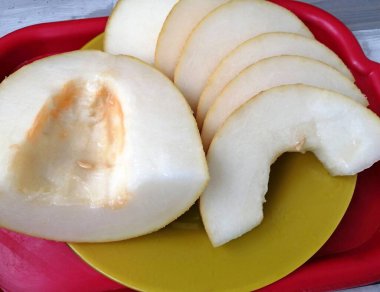 Sulu kavun, büyük dilimlere bölünmüş, sarı bir tabağa serilmiş. İştah açıcı bir vejetaryen yemeği kırmızı bir tepsiye konur. fotoğrafçılık üst görünümü.