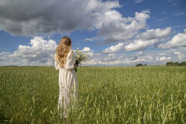 Buğdaylı tarlada elinde papatya buketi olan bir kız..