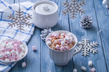 Mavi ahşap arka planda lokum ve Noel süslemeleri olan bir fincan lezzetli sıcak kakao..