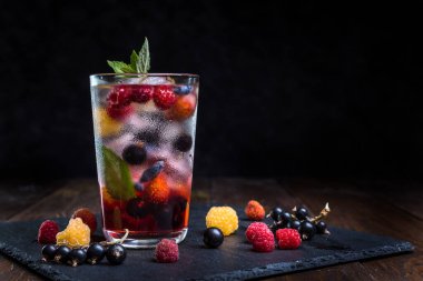 Siyah arka planda şeffaf bir bardakta çilekli limonata..