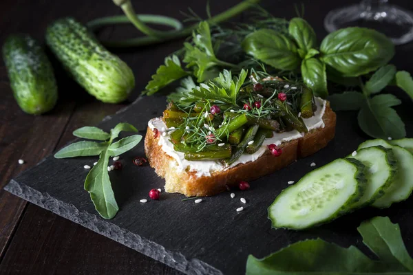 Toast with curd cheese, fried garlic arrows and herbs on a dark background.