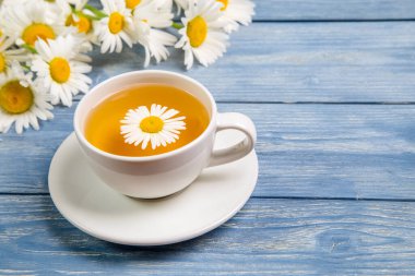 Papatya çiçeklerinden bitki çayı ve mavi arka planda bir buket papatya. Sağlıklı çay kavramı.