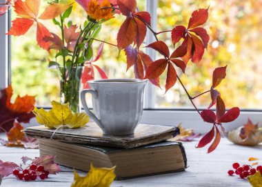 Ahşap pencere eşiğinde bir fincan çay ve doğal arka planda bir buket sonbahar yaprağı.. 
