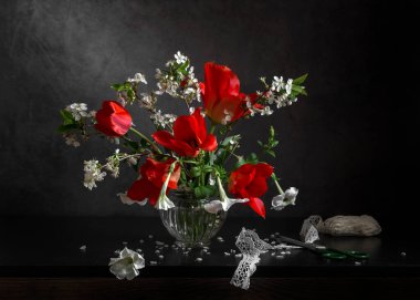 Kırmızı laleler ve cam bir vazoda çiçek açan kiraz dalları. Bahar hala hayat.