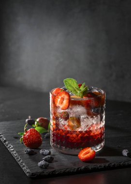 Soğuk, ev yapımı, cam bardakta buzlu çilekli limonata, koyu arkaplanda nane yaprakları ve meyveler..