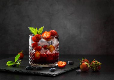 Soğuk, ev yapımı, cam bardakta buzlu çilekli limonata, koyu arkaplanda nane yaprakları ve meyveler..