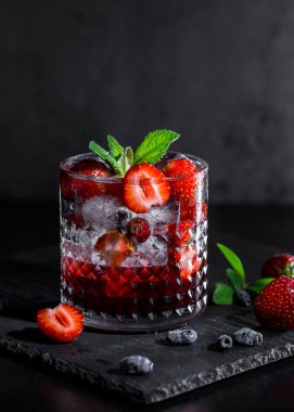 Soğuk, ev yapımı, cam bardakta buzlu çilekli limonata, koyu arkaplanda nane yaprakları ve meyveler..