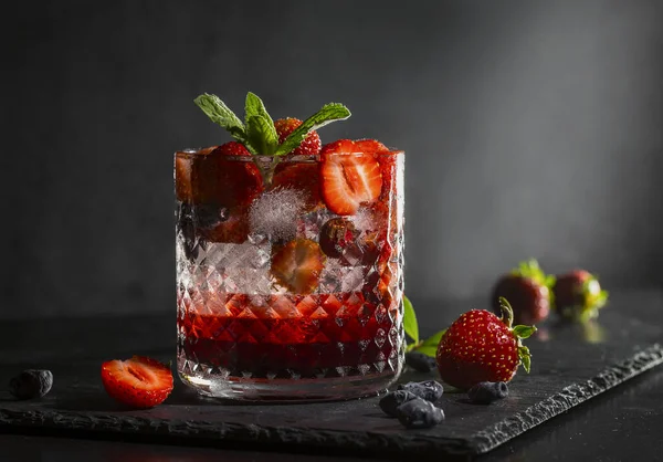 Soğuk, ev yapımı, cam bardakta buzlu çilekli limonata, koyu arkaplanda nane yaprakları ve meyveler..