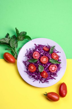 Domatesli kırmızı lahana salatası ve sarı-yeşil arka planda bir tabakta fesleğen. Boşluğu kopyala.