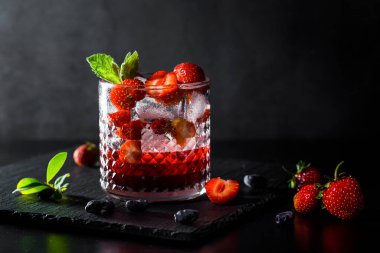 Soğuk, ev yapımı, cam bardakta buzlu çilekli limonata, koyu arkaplanda nane yaprakları ve meyveler..