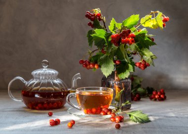 Şeffaf bir fincanda dikenli sıcak çay ve arka planda çay olan çaydanlık..