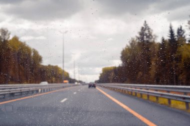 Arabanın ön camından yol manzarası ve sürat yaparken yağmur damlaları. Odaklanmamış otoyol. Sonbahar