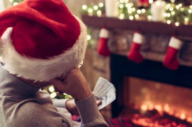 Noel Baba şapkalı üzgün adam Noel ağacı ve şöminenin yanında oturmuş Amerikan dolarlarını saymayı düşünüyor. Noel zamanı hediye almak için para harcıyorsun. konsept.