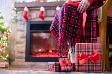 Koltuğunda oturan engelli kadınların çorapları şöminenin yanındaki ekoseyle kaplı ve Noel ağacı ve aile için hediye paketleri. Alt görünüm.